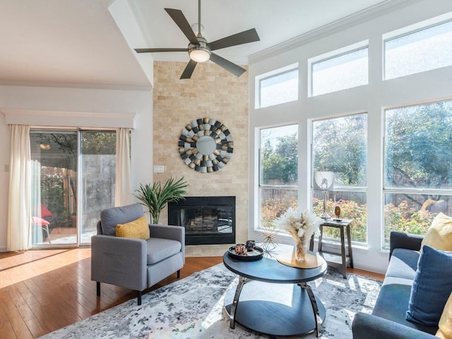 living area featuring a glass covered fireplace, crown molding, wood-type flooring, and ceiling fan