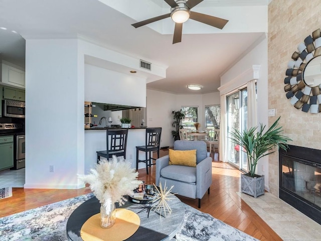 living area featuring visible vents, a tile fireplace, ceiling fan, and wood finished floors