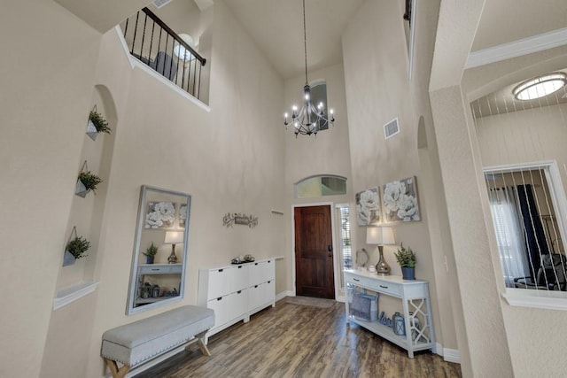 entrance foyer with a notable chandelier, wood finished floors, visible vents, and arched walkways