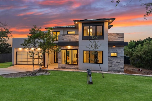 view of front facade featuring concrete driveway, stucco siding, a yard, stone siding, and a standing seam roof