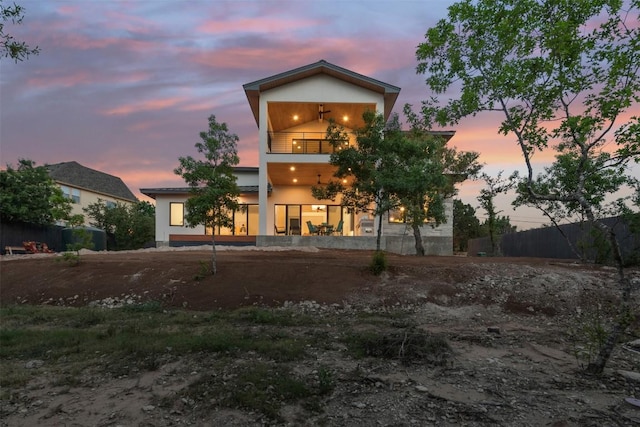 back of house at dusk with a balcony and stucco siding