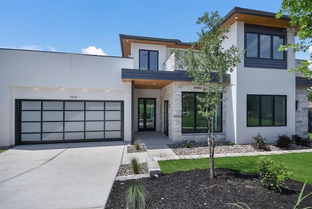 modern home featuring stucco siding, stone siding, an attached garage, and driveway