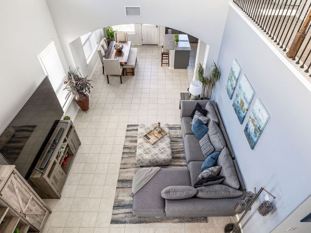 living area with light tile patterned floors, arched walkways, visible vents, and a towering ceiling