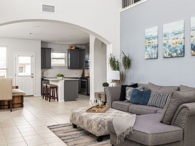 living area featuring light tile patterned flooring, arched walkways, and visible vents