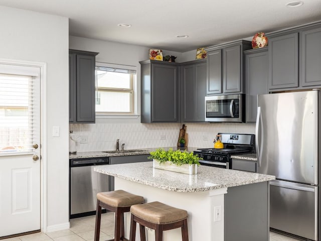 kitchen with light stone counters, a kitchen island, a sink, appliances with stainless steel finishes, and backsplash