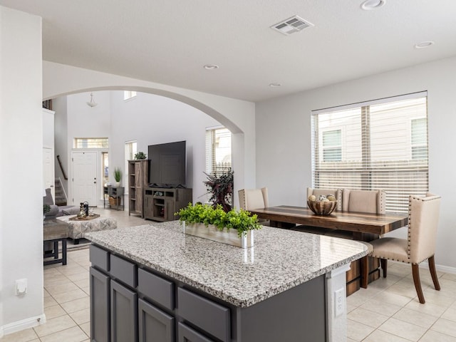 248 Brady Creek Way, Leander, TX 78641 - kitchen with gray cabinets, arched walkways, light stone counters, light tile patterned floors, and a kitchen island