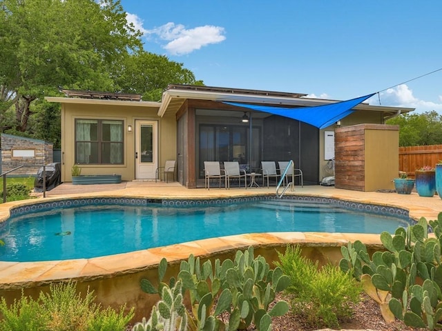 rear view of property with fence, an outdoor pool, a sunroom, stucco siding, and a patio area