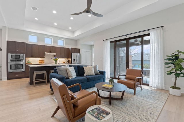 living area with visible vents, ceiling fan, a tray ceiling, recessed lighting, and light wood-style flooring