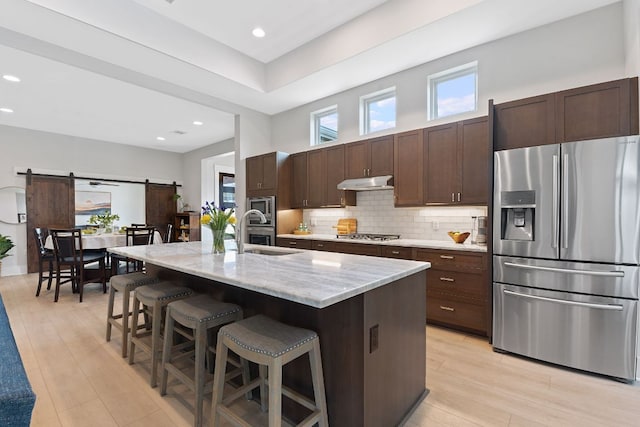 kitchen featuring a sink, stainless steel appliances, under cabinet range hood, a barn door, and tasteful backsplash