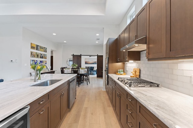 kitchen with stainless steel appliances, a sink, wine cooler, under cabinet range hood, and a barn door