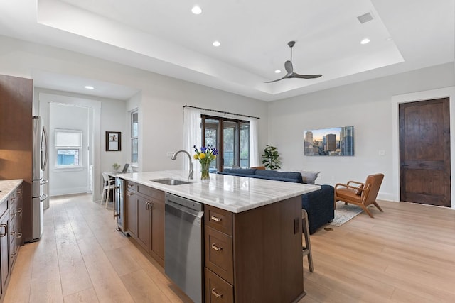 kitchen featuring stainless steel appliances, light wood-type flooring, a tray ceiling, and a sink