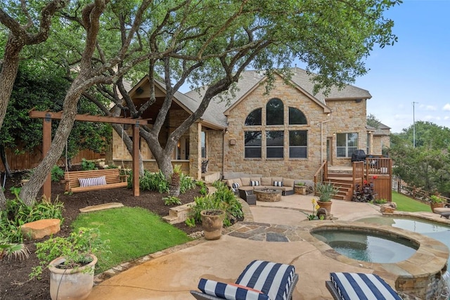 rear view of house with a deck, stone siding, a patio, a fire pit, and an in ground hot tub