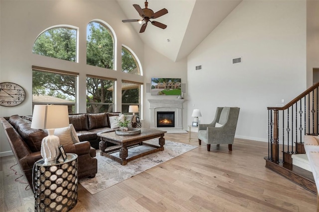 living area featuring visible vents, ceiling fan, stairs, wood finished floors, and a glass covered fireplace