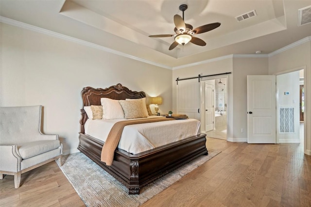 bedroom with a raised ceiling, a barn door, and light wood finished floors