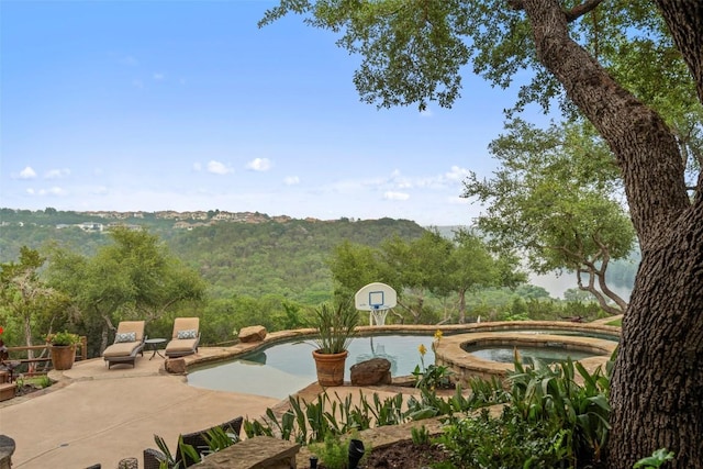 exterior space featuring an in ground hot tub, a view of trees, and an outdoor pool