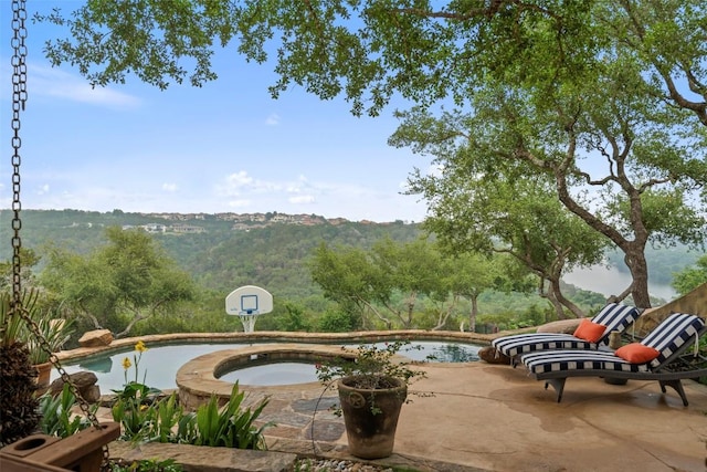 view of community featuring a pool, a patio area, a jacuzzi, and a view of trees