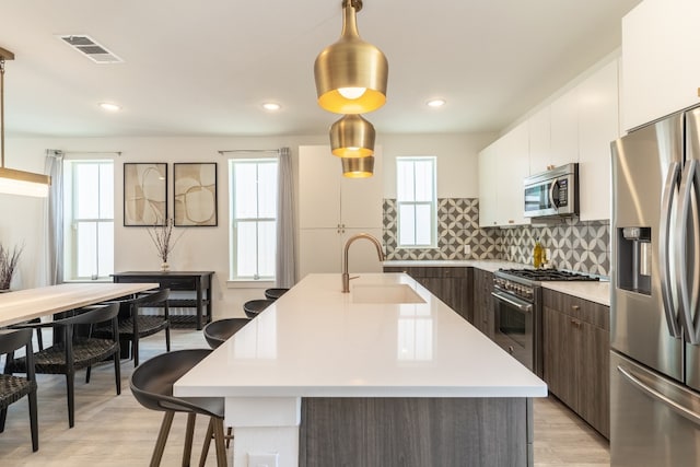 kitchen with light countertops, stainless steel appliances, hanging light fixtures, modern cabinets, and a sink