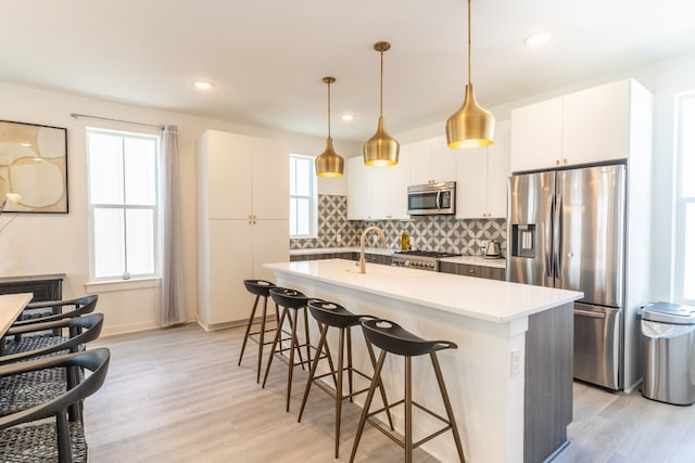 kitchen with light wood-style flooring, stainless steel appliances, light countertops, a kitchen bar, and backsplash