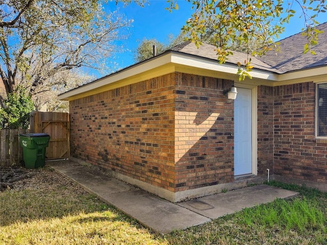 doorway to property with brick siding, fence, and roof with shingles