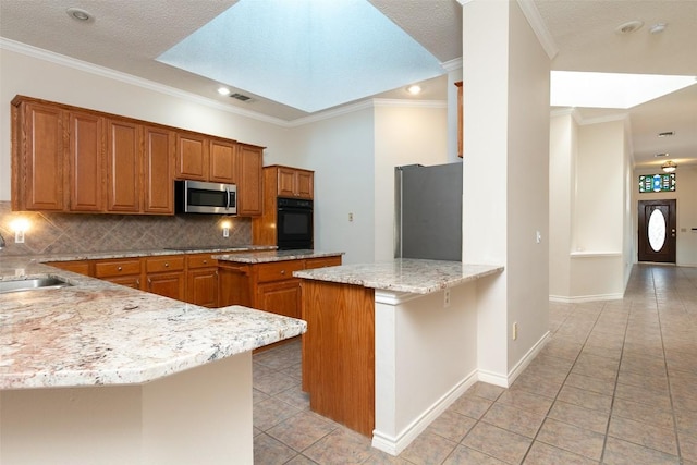 kitchen featuring tasteful backsplash, light stone countertops, a peninsula, brown cabinetry, and black appliances