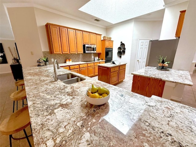 kitchen with black appliances, a sink, a kitchen island, a skylight, and crown molding