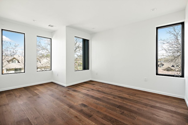 unfurnished room featuring visible vents, baseboards, and dark wood-style floors