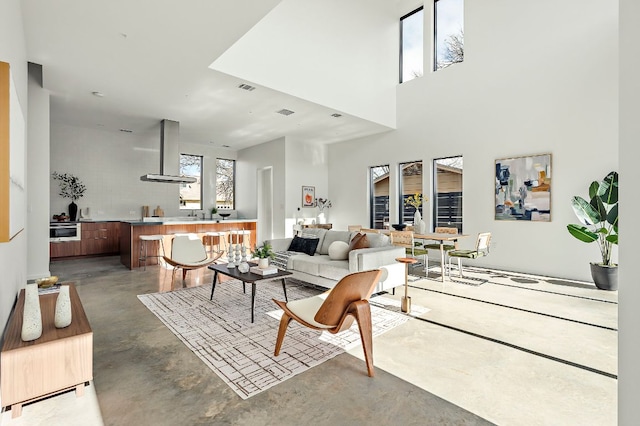 living area with visible vents, concrete flooring, and a towering ceiling