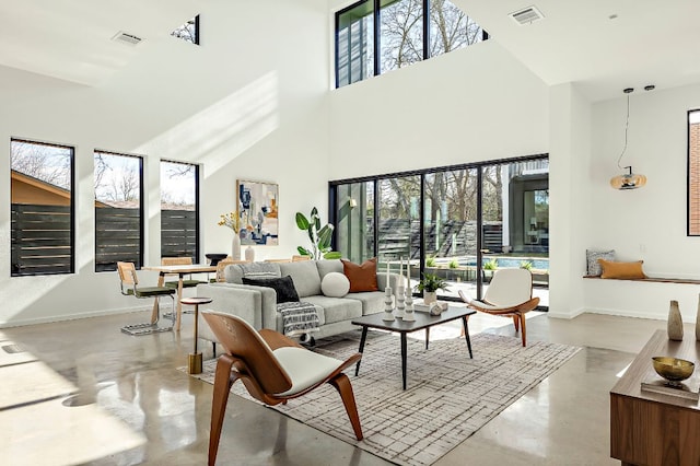 living area with a towering ceiling, baseboards, visible vents, and concrete flooring