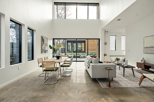 living room with finished concrete flooring, a towering ceiling, and baseboards