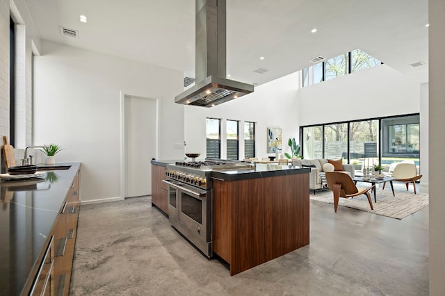 kitchen with modern cabinets, range with two ovens, island exhaust hood, concrete floors, and a towering ceiling