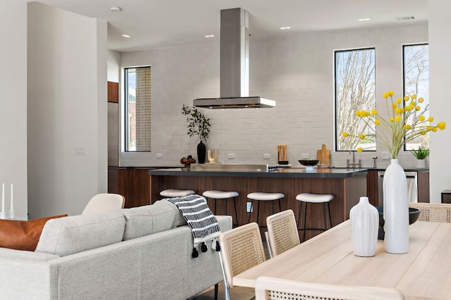 kitchen with exhaust hood, backsplash, dark countertops, a kitchen breakfast bar, and recessed lighting