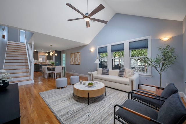 living area with baseboards, ceiling fan, stairs, wood finished floors, and high vaulted ceiling