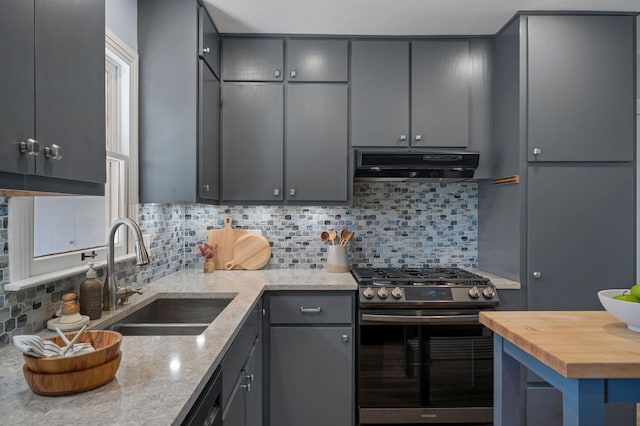 kitchen with ventilation hood, decorative backsplash, gray cabinets, stainless steel gas range, and a sink