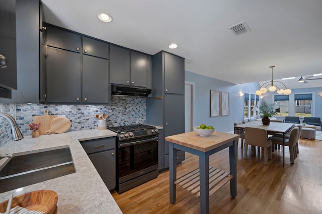 kitchen featuring visible vents, a sink, light wood-style floors, under cabinet range hood, and gas range