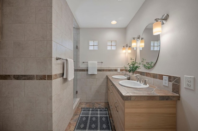 bathroom with a tile shower, double vanity, tile walls, and a sink