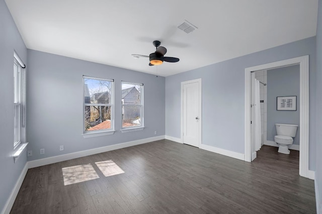 unfurnished bedroom featuring visible vents, dark wood-type flooring, ensuite bathroom, baseboards, and ceiling fan