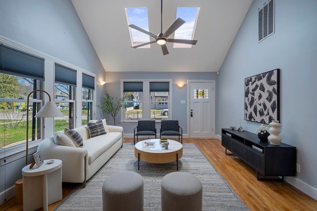 living room featuring a ceiling fan, a skylight, light wood-style flooring, and high vaulted ceiling