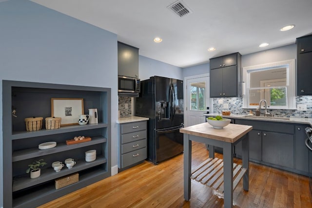 kitchen with stainless steel microwave, gray cabinetry, light countertops, black fridge, and a sink