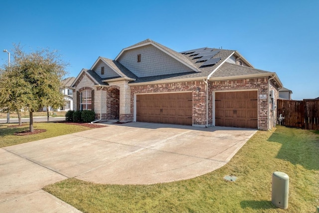 view of front facade featuring driveway, solar panels, an attached garage, a shingled roof, and a front lawn