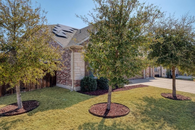 view of front of property featuring stone siding, solar panels, concrete driveway, and a front lawn