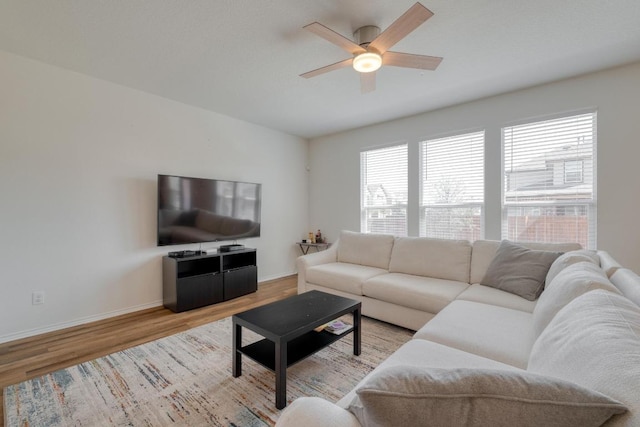 living area featuring wood finished floors, a healthy amount of sunlight, baseboards, and ceiling fan