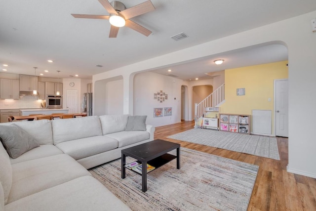 living room featuring visible vents, ceiling fan, stairs, light wood-style floors, and arched walkways