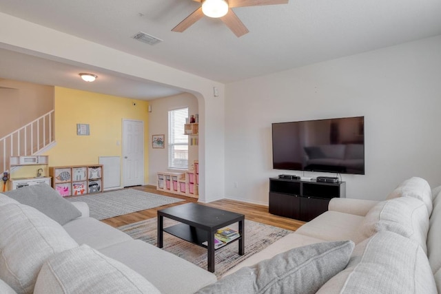 living area featuring a ceiling fan, wood finished floors, visible vents, arched walkways, and stairs