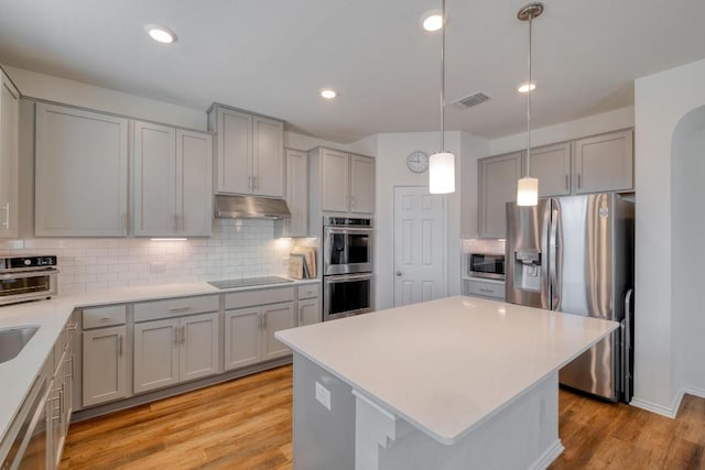 1004 Brenham Ln, Leander, TX 78641 - kitchen with stainless steel appliances, gray cabinetry, under cabinet range hood, backsplash, and light wood finished floors