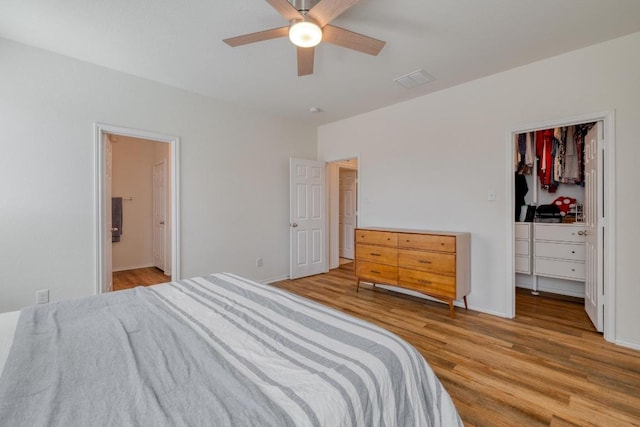 bedroom featuring a ceiling fan, wood finished floors, a spacious closet, a closet, and connected bathroom