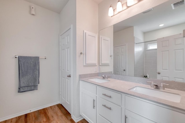 full bath with a tile shower, visible vents, wood finished floors, and a sink