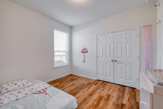 bedroom featuring light wood-type flooring, baseboards, and a closet