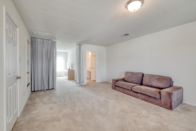 living area with visible vents, light colored carpet, and a textured ceiling