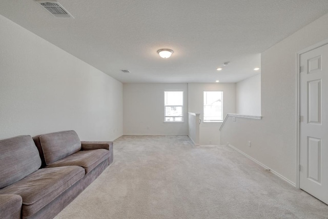 living area with visible vents, light colored carpet, a textured ceiling, and baseboards