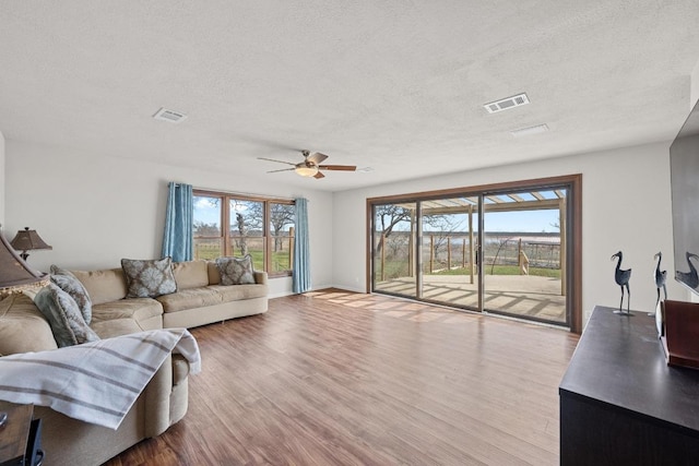 living area featuring a textured ceiling, wood finished floors, visible vents, and ceiling fan